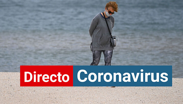 Une femme portant un masque de coronavirus se promène le long de la plage.