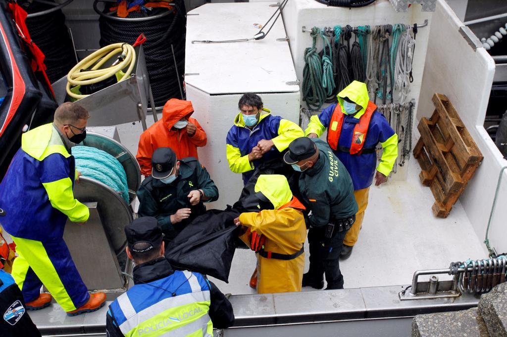 Des agents de la Garde civile et des marins déplacent le corps d'un des défunts.