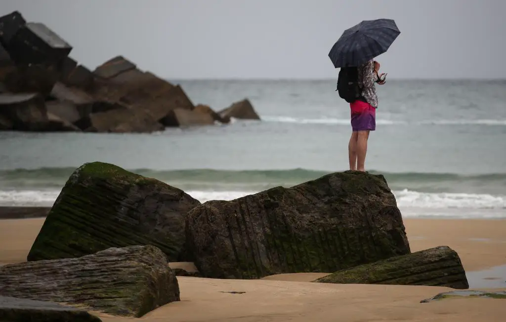 Un jeune homme se protège avec un parapluie sur la plage de Zurriola à San Sebasti