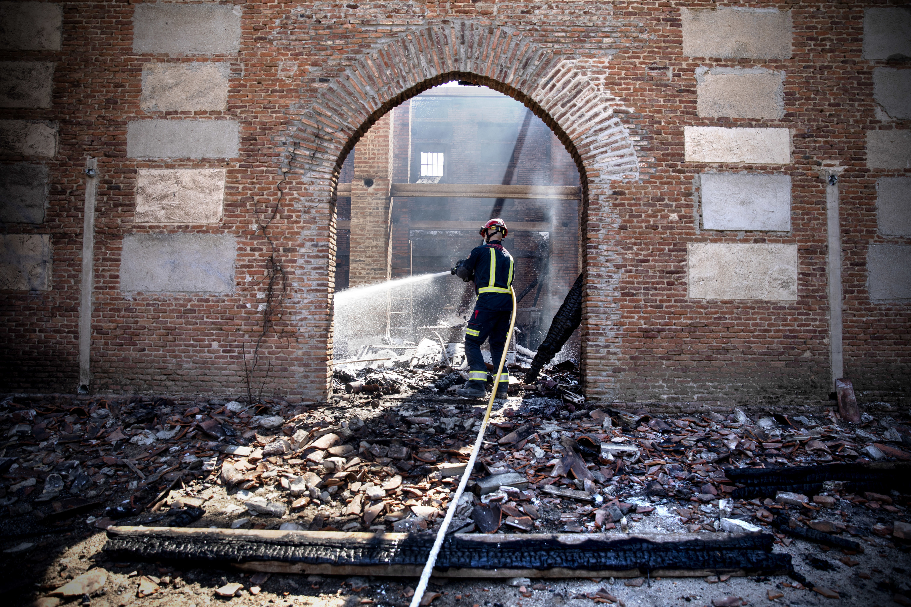 Un pompier éteint les braises avec son tuyau dans le vieux séchoir à tabac.