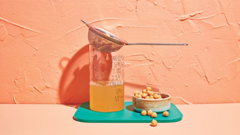 Un verre doseur d'aquafaba, à côté d'un bol de pois chiches.