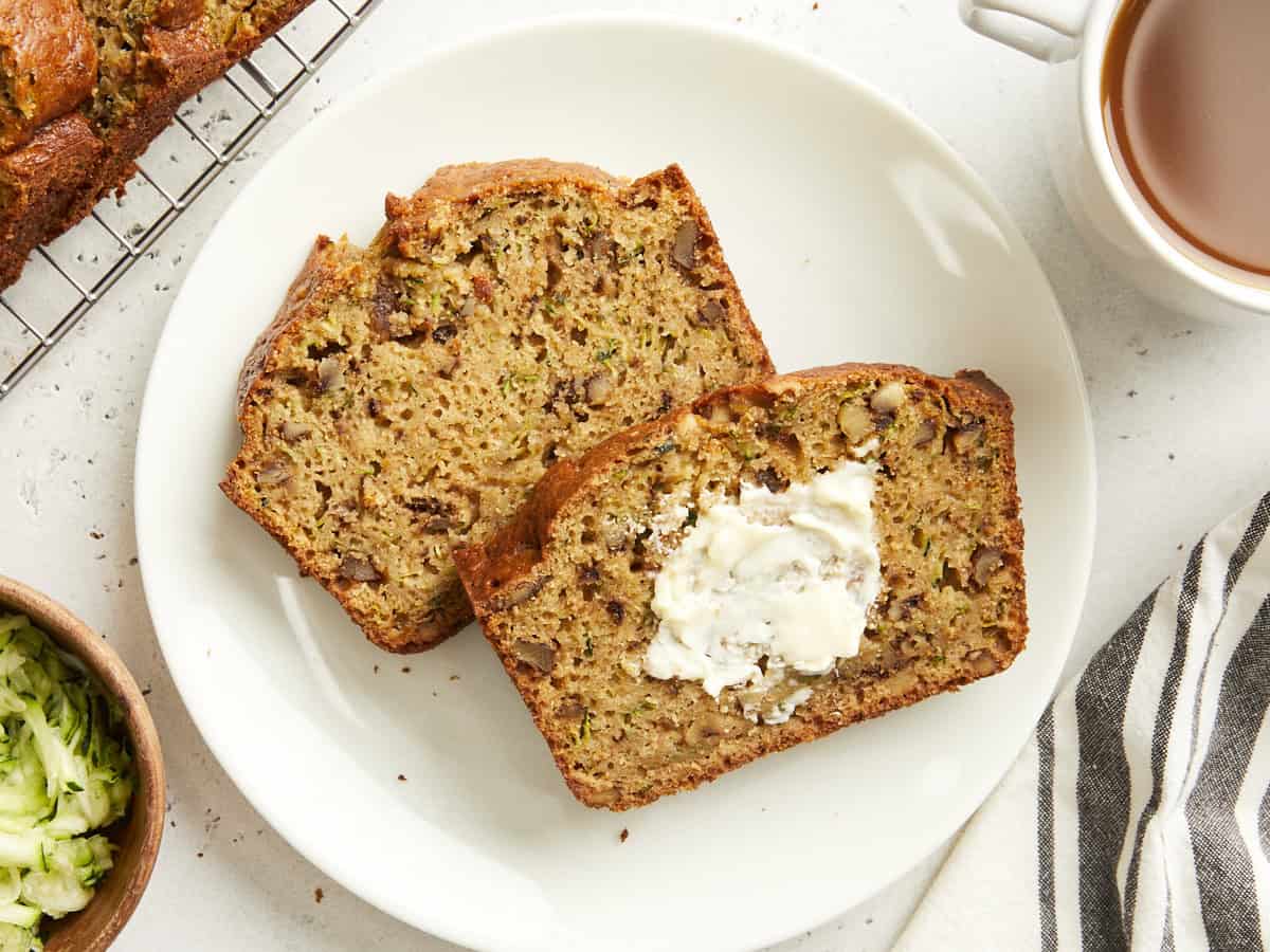 Deux tranches de pain aux courgettes sur une assiette blanche avec du beurre tartiné sur une tranche.
