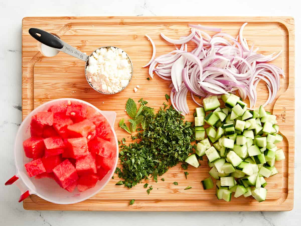 mise en place d'une salade de pastèque et de feta sur une planche à découper en bois.