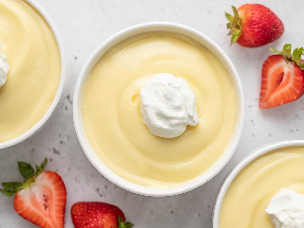 Vue aérienne d'un pudding à la vanille dans un bol blanc garni d'une cuillerée de crème fouettée et entouré de fraises.