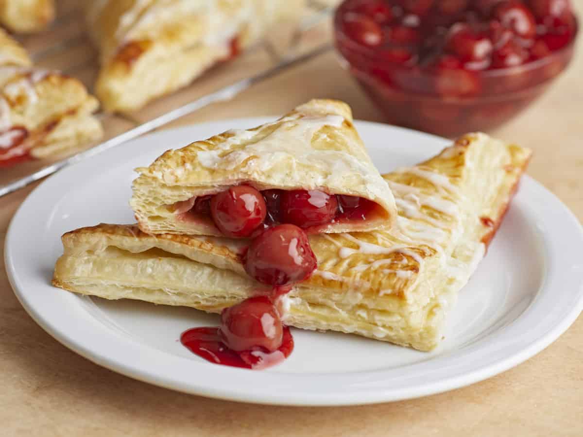 Deux chaussons aux cerises empilés sur une assiette, l'un coupé en deux avec la garniture qui déborde.