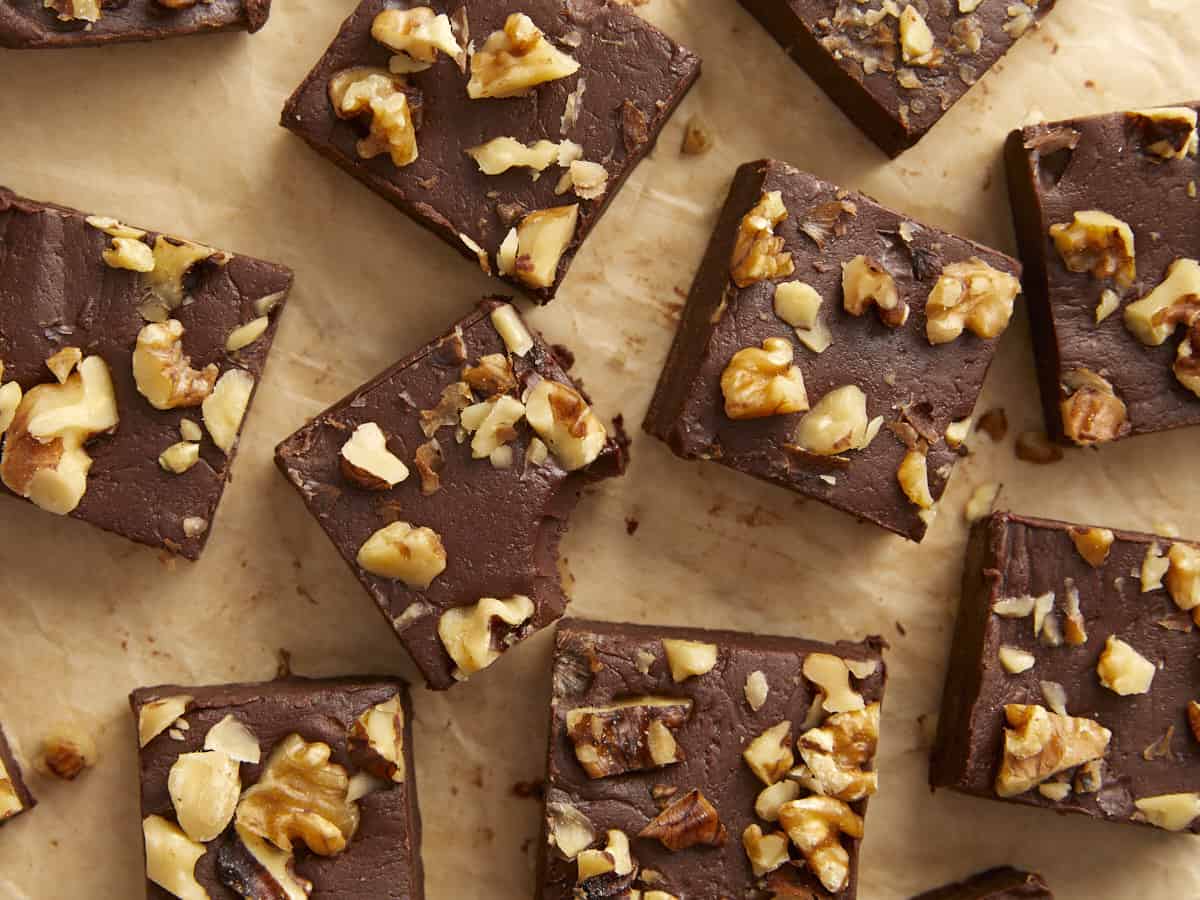 Vue aérienne de fudge au chocolat avec des noix coupées en carrés sur une surface en bois, l'un avec une bouchée retirée.