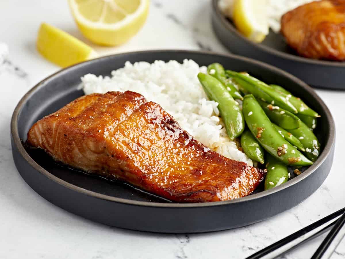 vue latérale d'une portion de saumon à la friteuse à air sur une assiette noire avec du riz et des pois.
