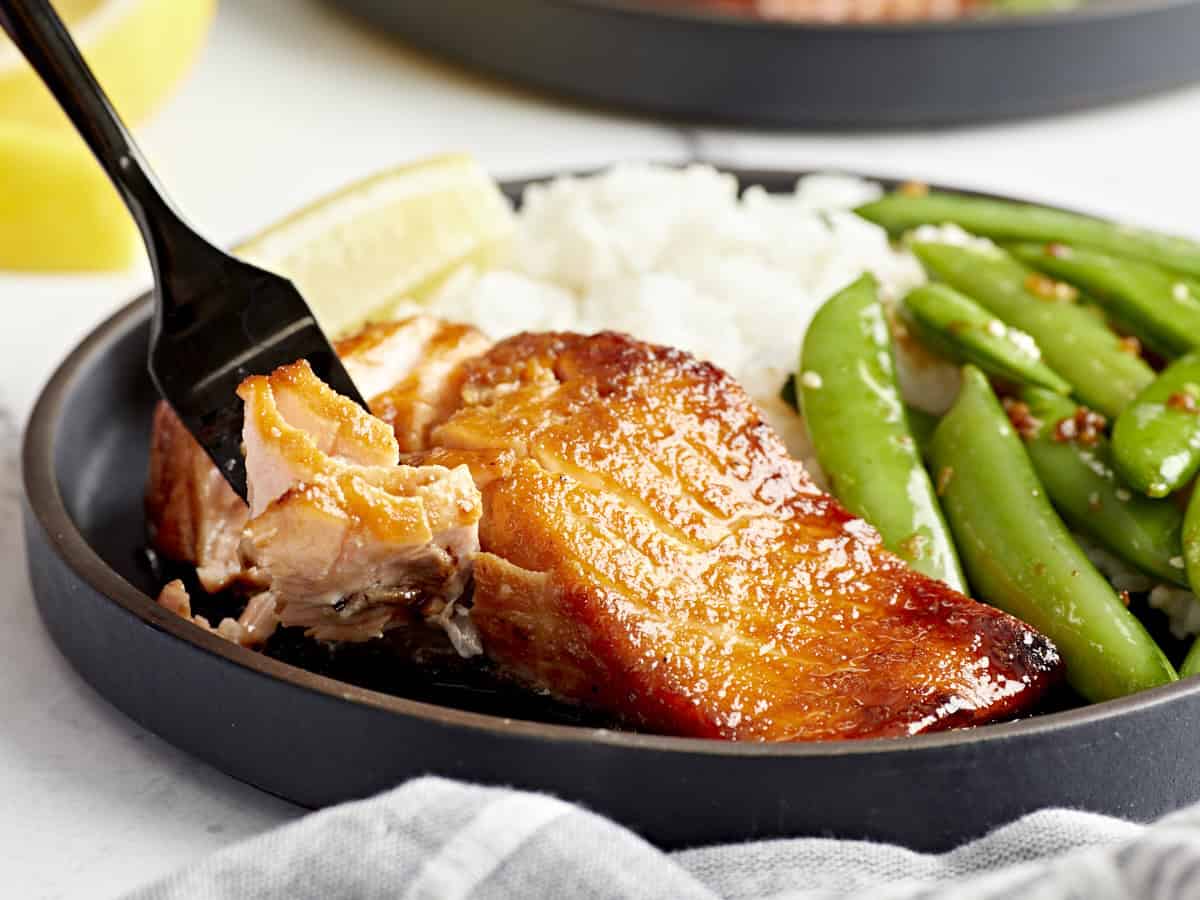 une fourchette de saumon à la friteuse à air devant une portion dans une assiette avec du riz et des petits pois.