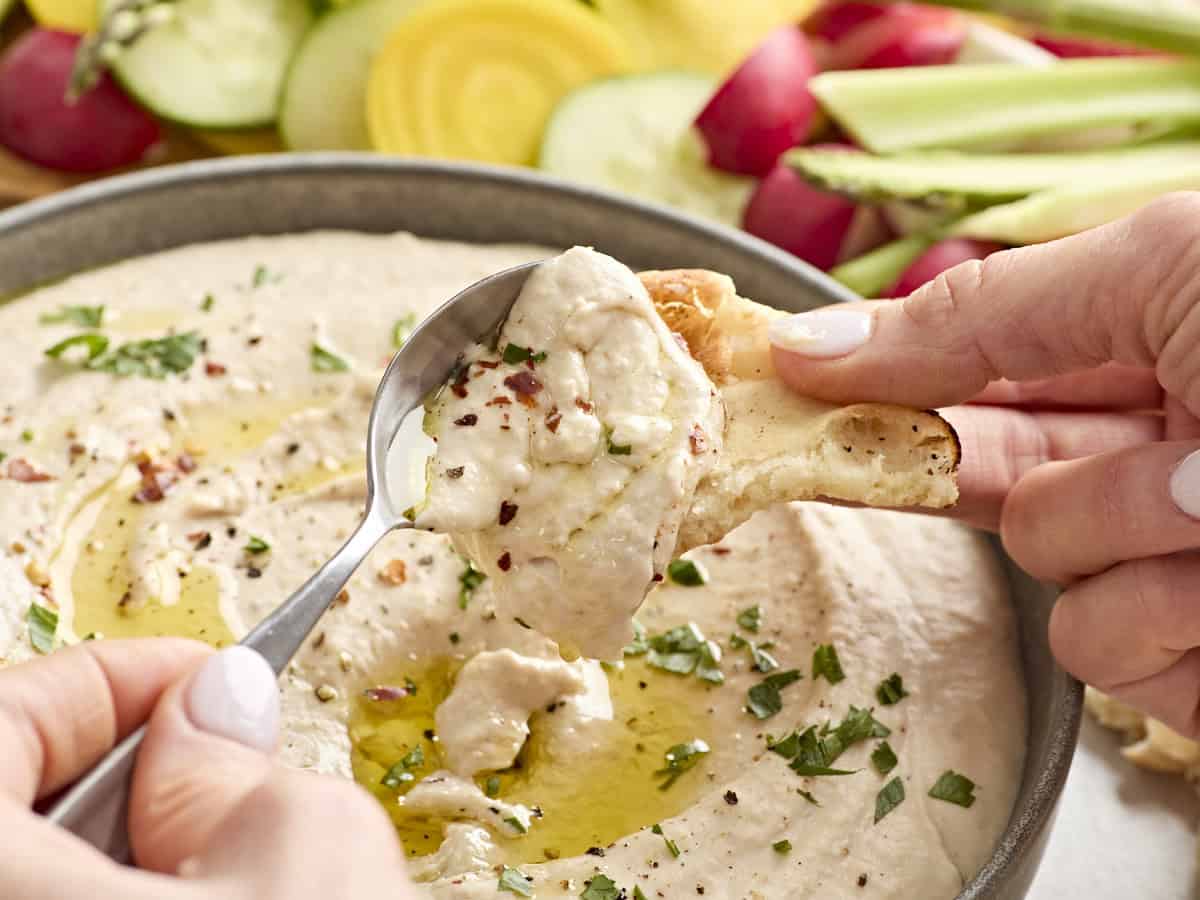 Une main déposant du houmous aux haricots blancs sur du pain pita