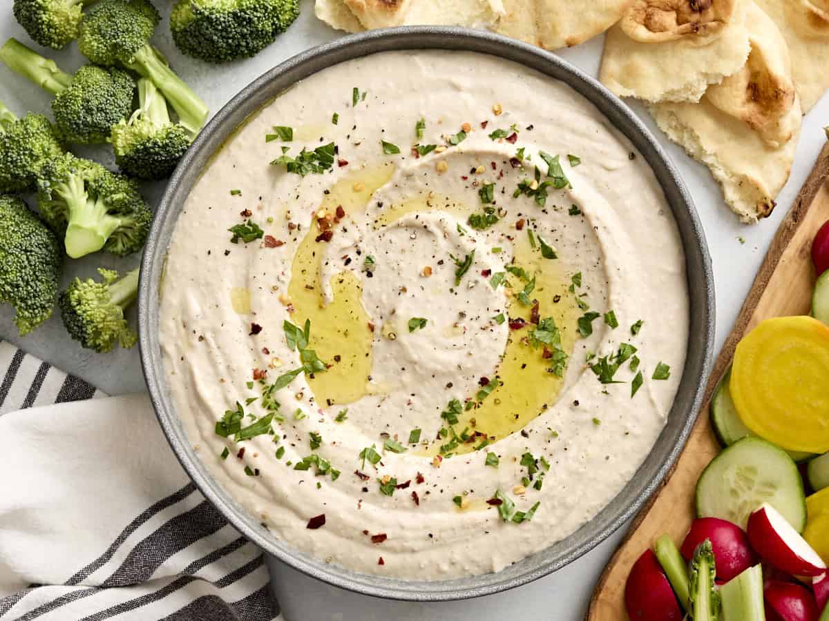 Un bol de houmous aux haricots blancs garni d'huile d'olive et d'herbes fraîches
