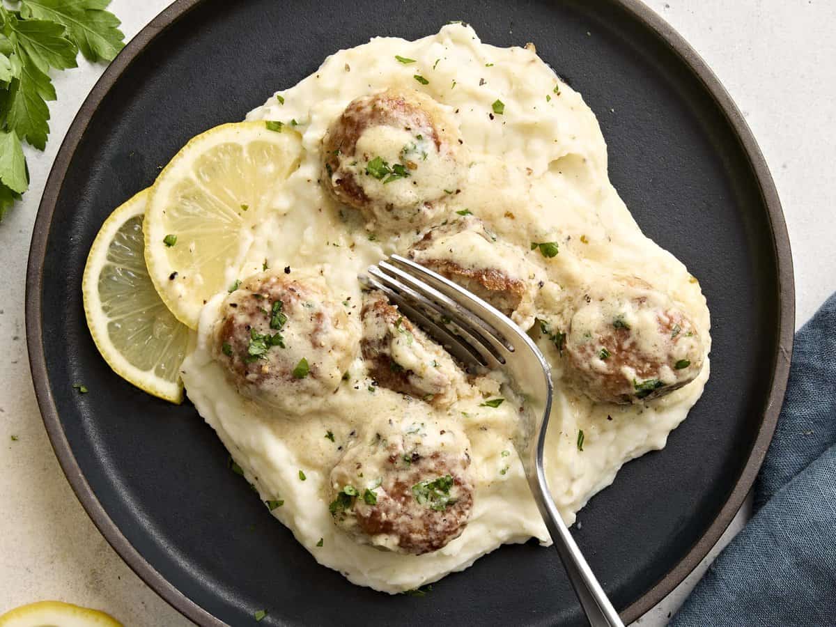 Vue aérienne de boulettes de poulet avec une sauce à la crème servies sur une assiette de purée de pommes de terre et une fourchette coupant une boulette de viande en deux.