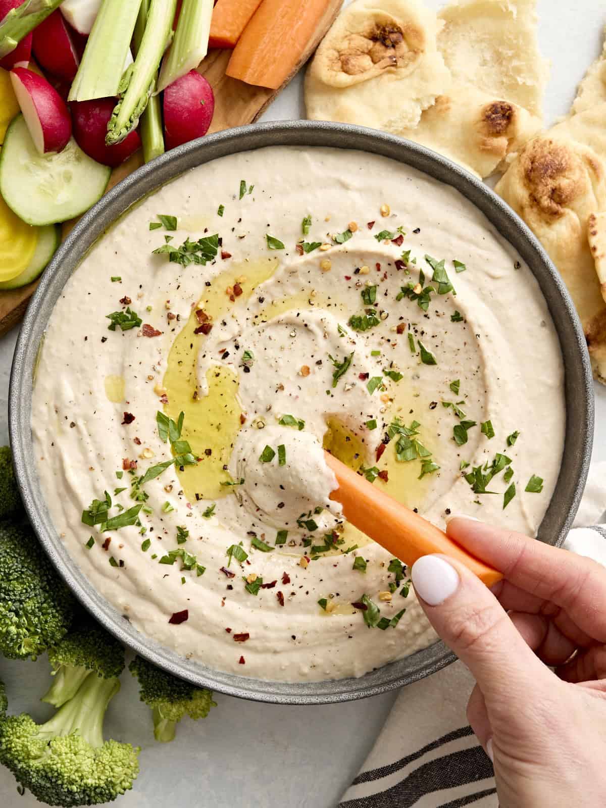Une main trempant un bâton de carotte dans un bol de houmous aux haricots blancs