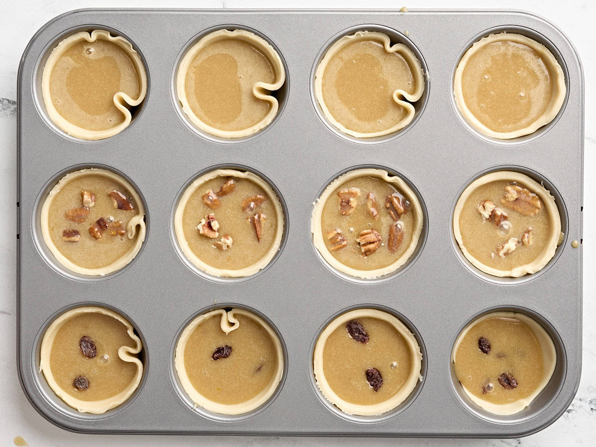 Croûtes à tarte dans un moule à cupcake rempli de garniture pour tarte au beurre.