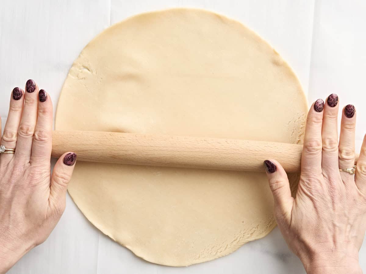 Mains utilisant un rouleau à pâtisserie pour étaler la croûte à tarte préfabriquée.