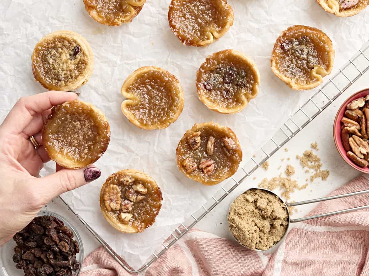Une main prenant une tarte au beurre sur une grille de refroidissement recouverte de papier sulfurisé.