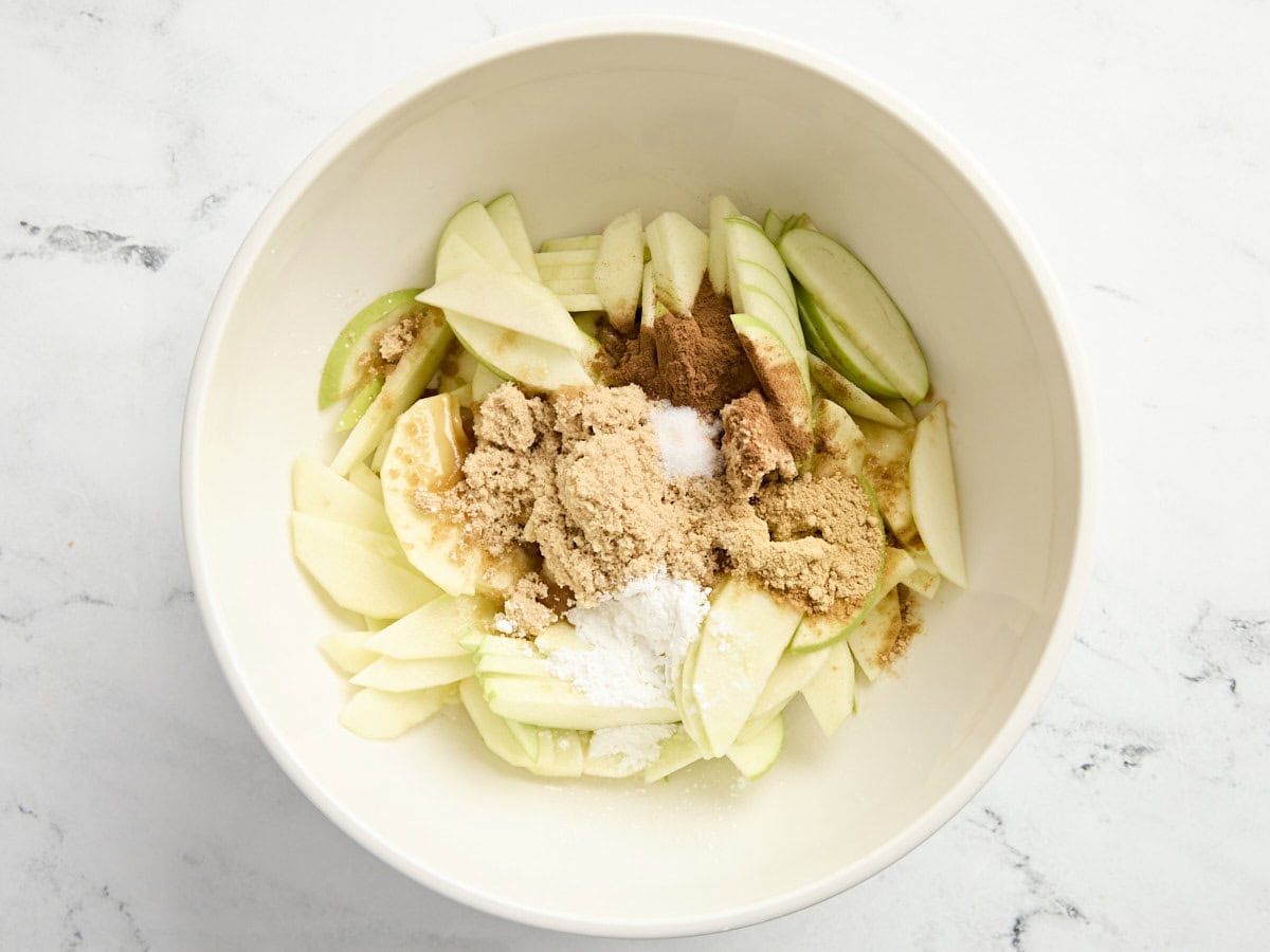 Pommes Granny Smith tranchées dans un bol à mélanger avec du sucre, de la fécule de maïs et de la cannelle.