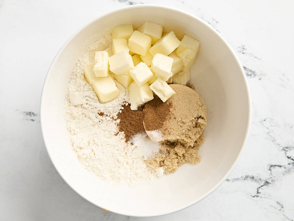 Beurre en cubes, farine, sucre et épices pour tarte à la citrouille dans un bol à mélanger.