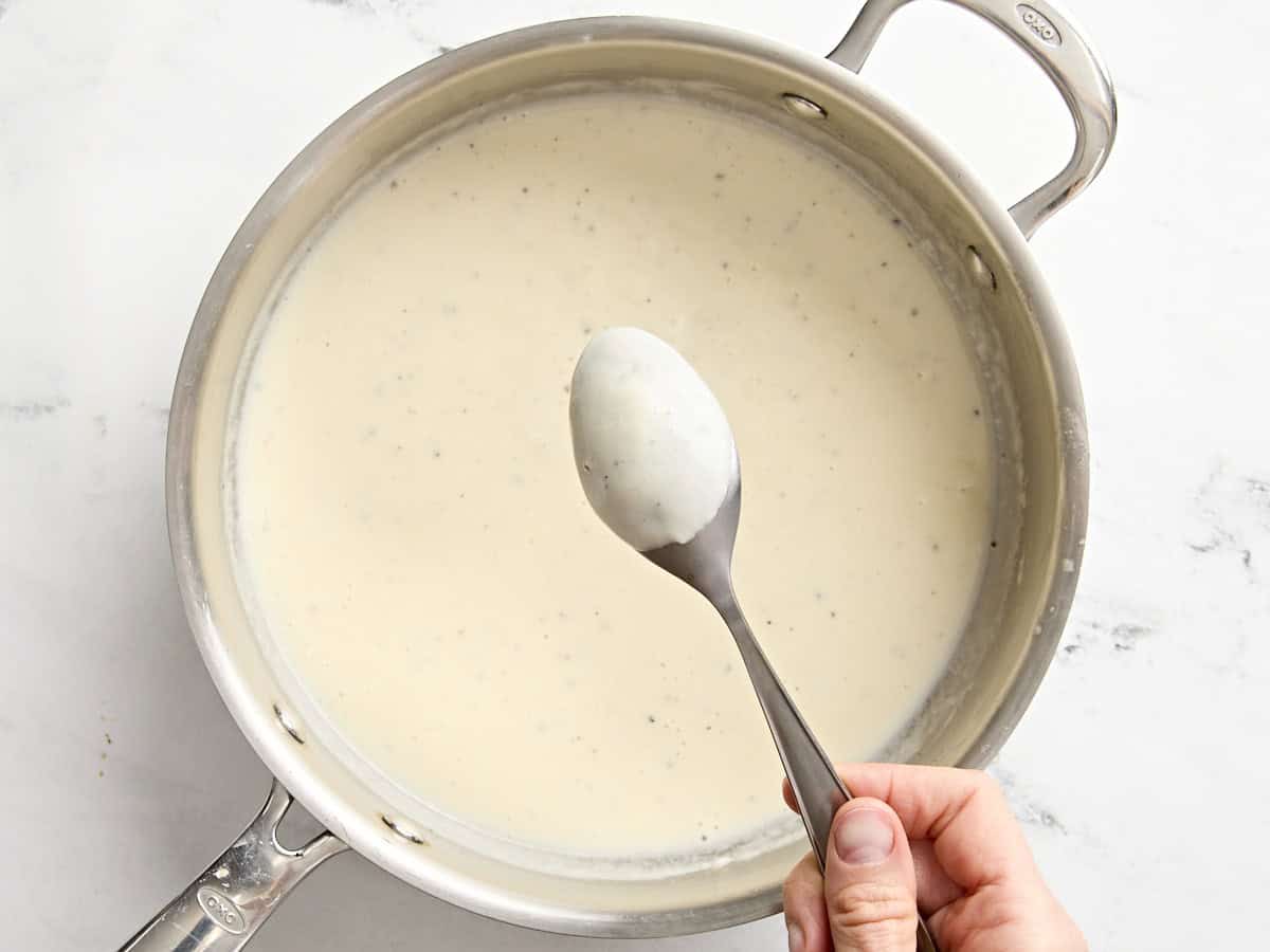 La sauce pour la crème de maïs dans une casserole avec une cuillère en vérifiant l'épaisseur.