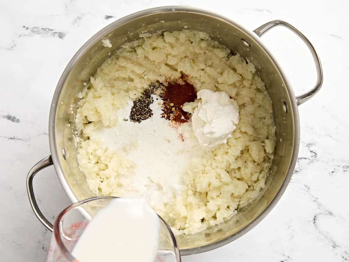 Assaisonnements, lait et crème sure ajoutés à une casserole avec purée de pommes de terre.