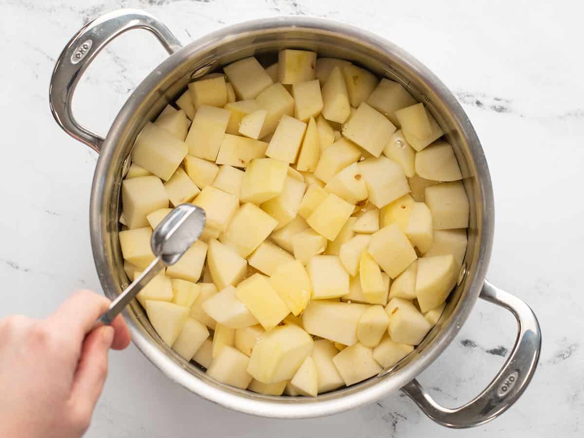 Du sel est ajouté à une casserole pleine de pommes de terre et d'eau.