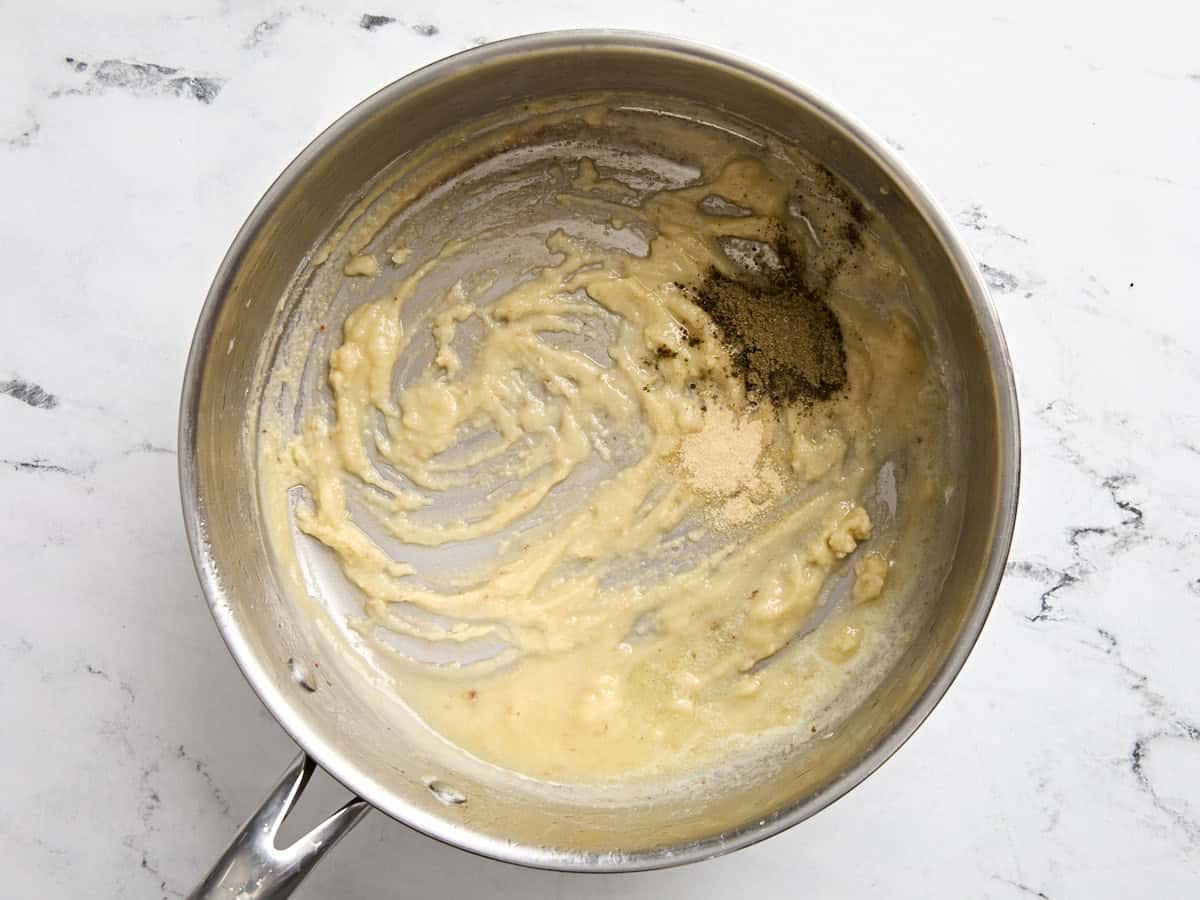 Assaisonnements ajoutés à un roux dans une casserole.