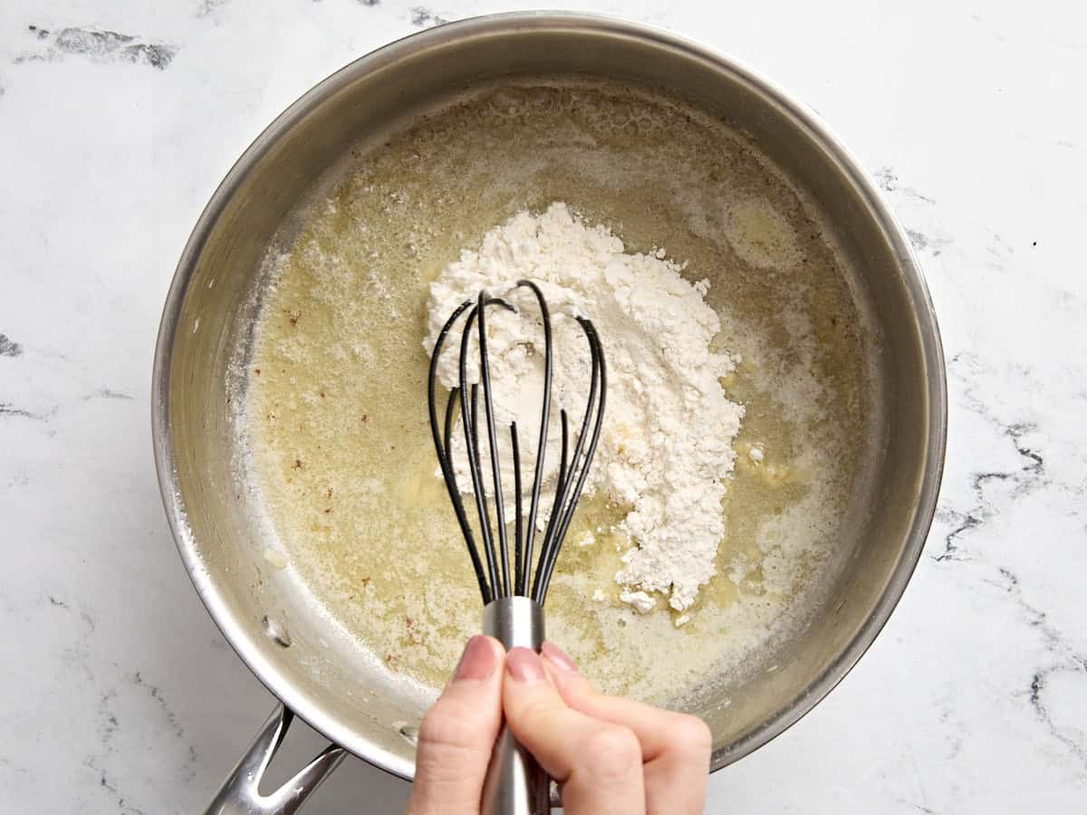 Une main fouettant la farine dans le beurre fondu dans une casserole.
