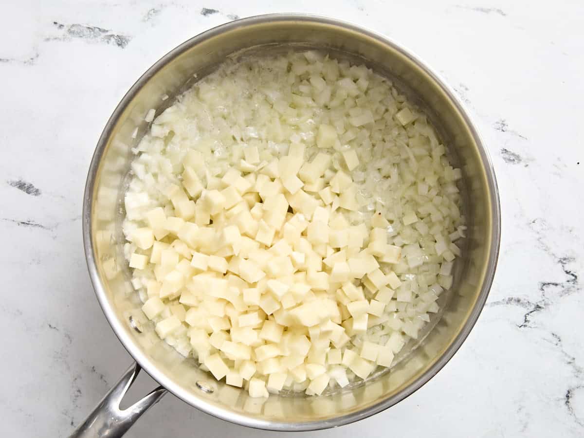 Pommes de terre coupées en dés ajoutées à la poêle avec les oignons et le beurre fondu.