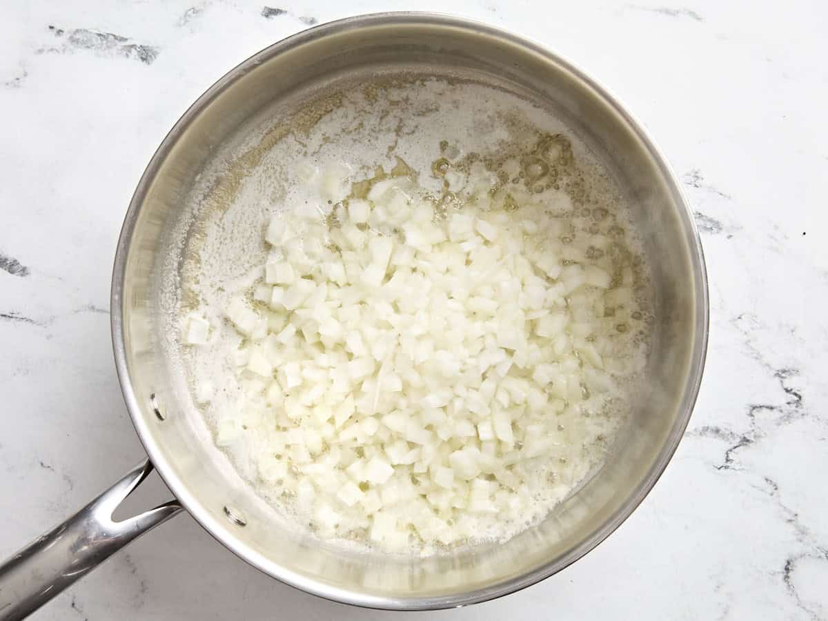 Oignon coupé en dés cuisant dans une poêle avec du beurre fondu.