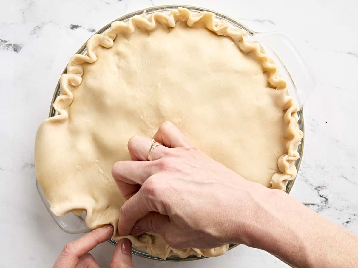 Une main sertissant les bords d’une croûte de tourte à la dinde.