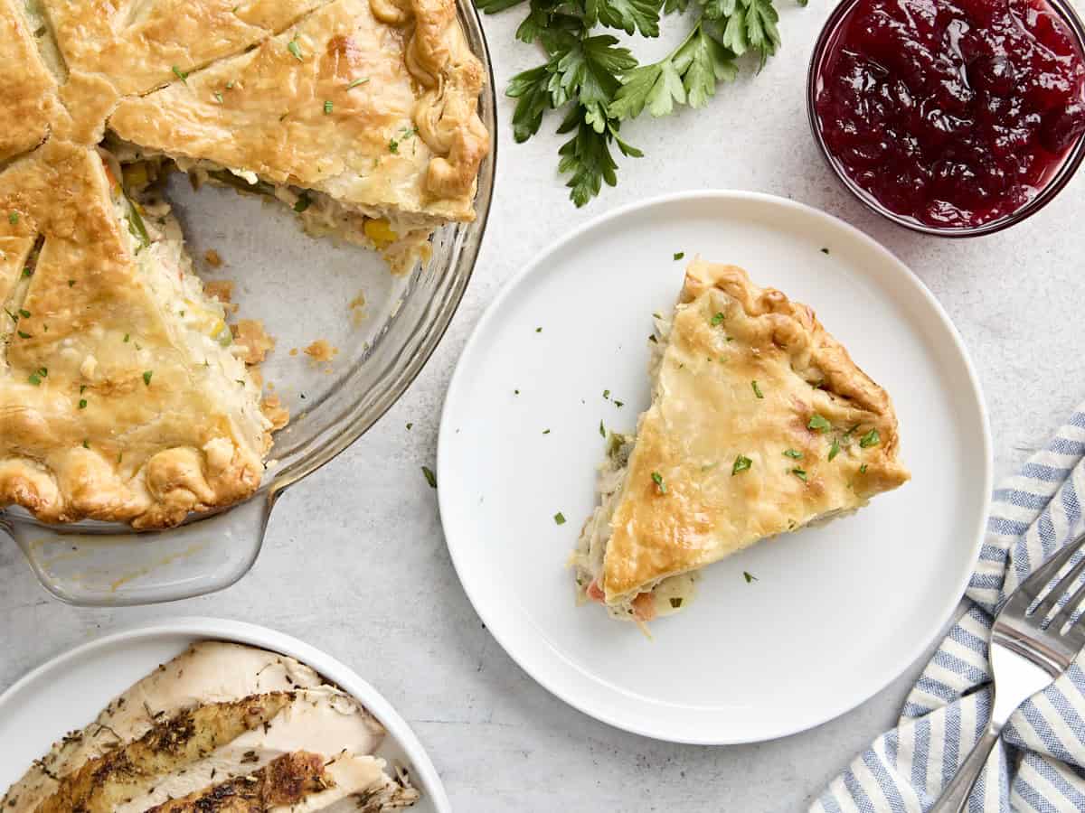 Vue aérienne d'une tranche de tourte à la dinde sur une assiette, à côté de la tarte restante dans un moule à tarte.