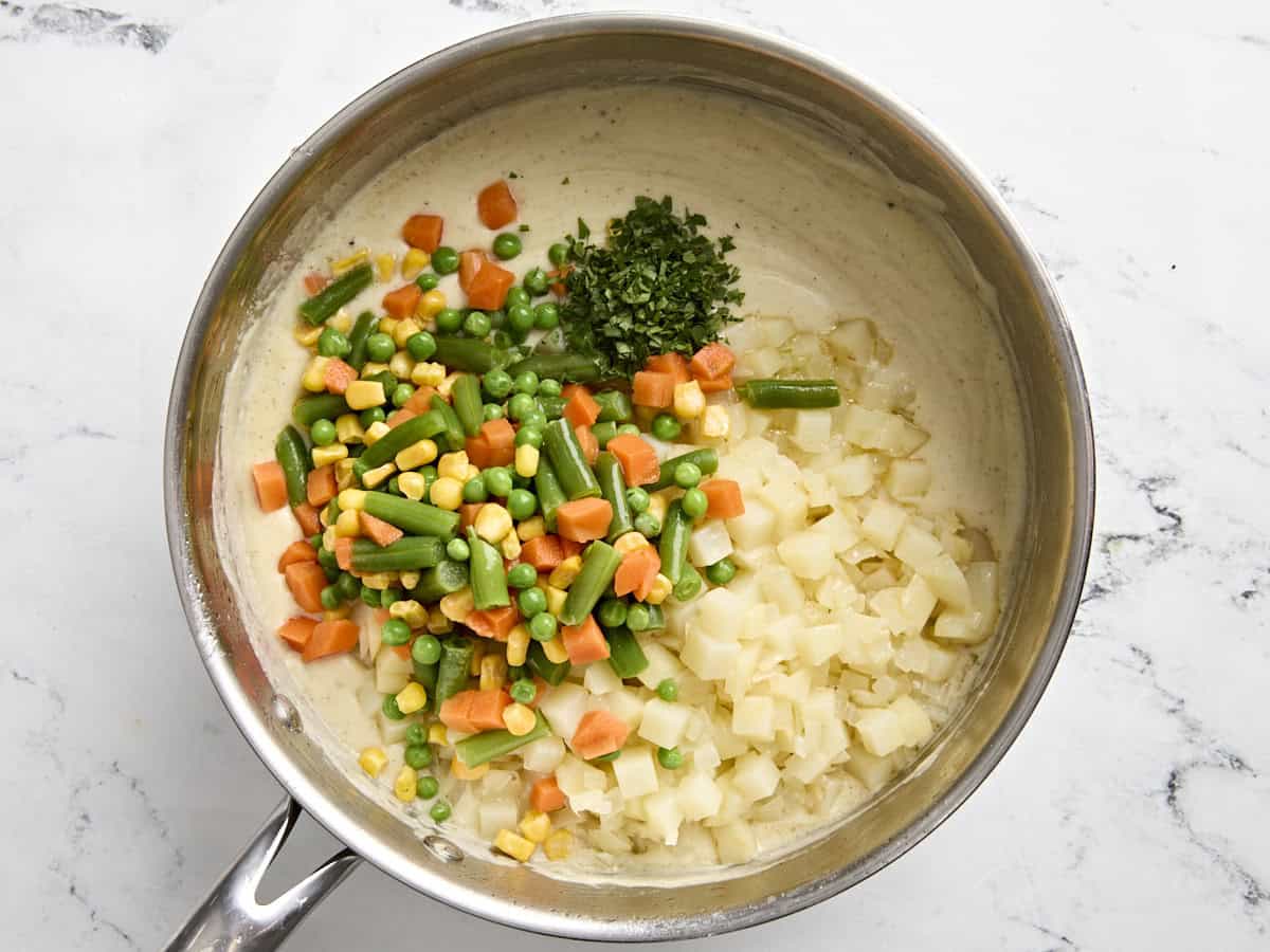 Pommes de terre coupées en dés et légumes mélangés ajoutés à la sauce crémeuse pour pâté à la dinde dans une casserole.
