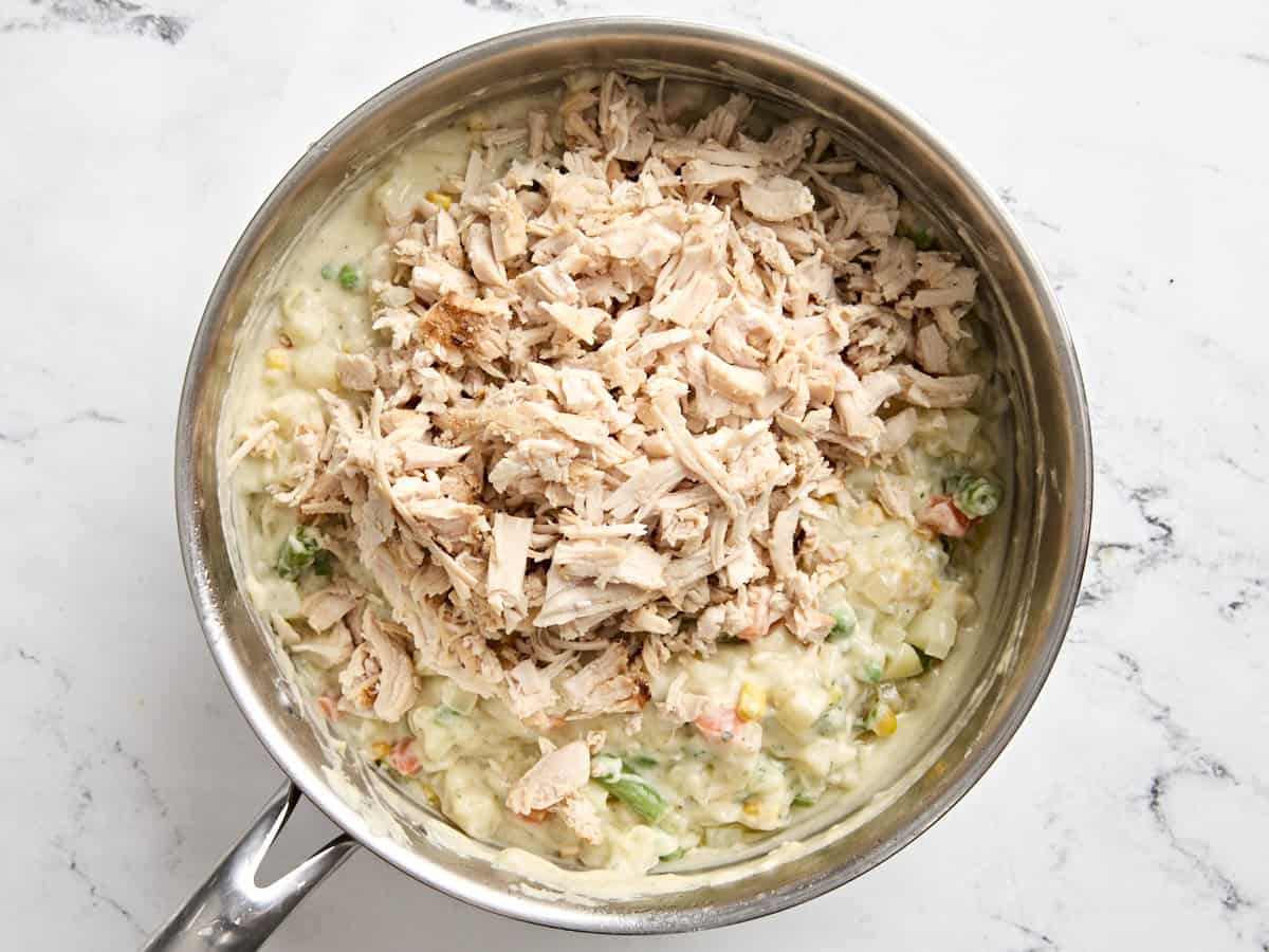 Dinde râpée ajoutée aux ingrédients de la tourte à la dinde dans une casserole.