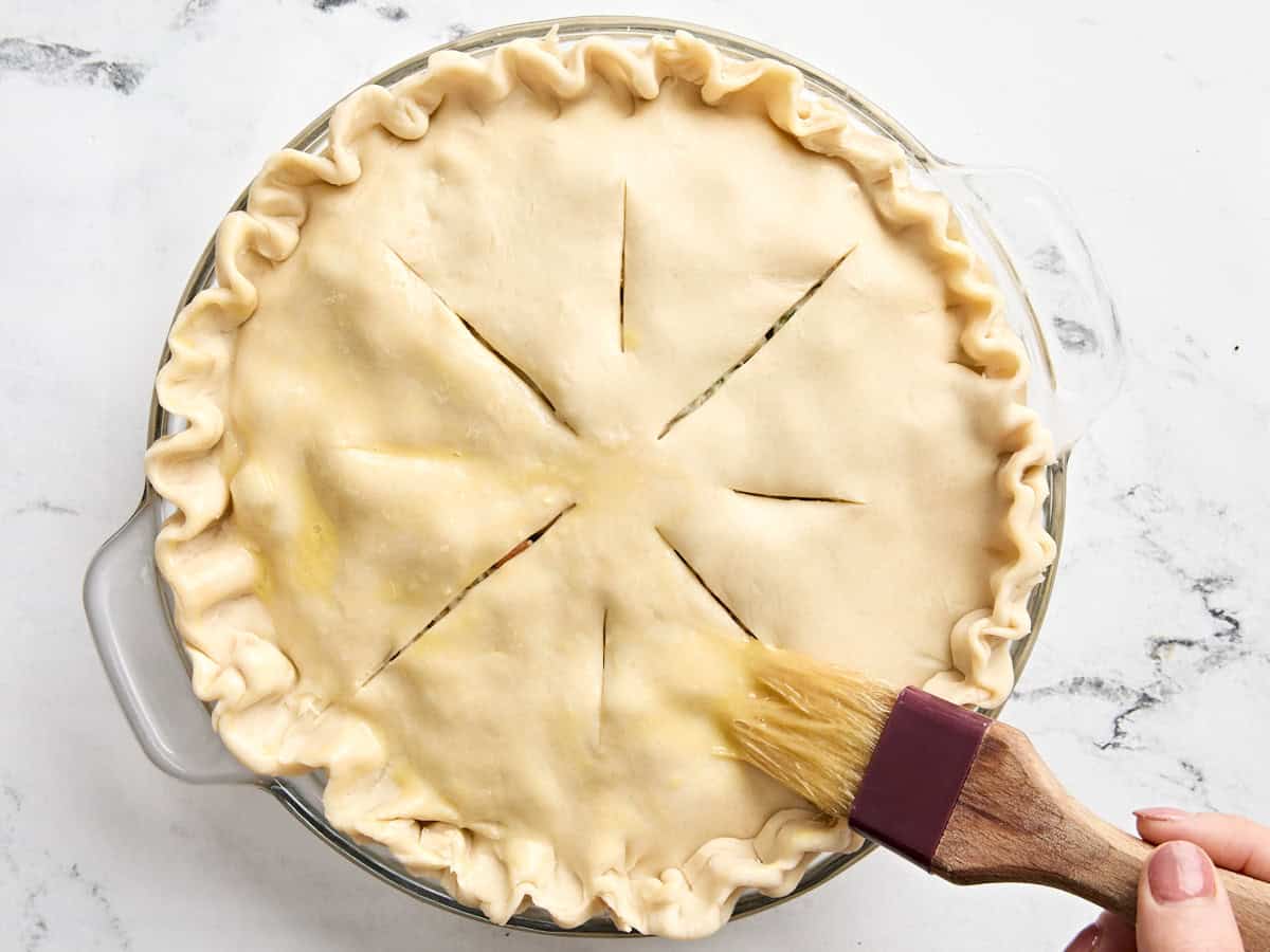 Un pinceau appliquant une dorure aux œufs sur la croûte non cuite d'une tourte à la dinde.