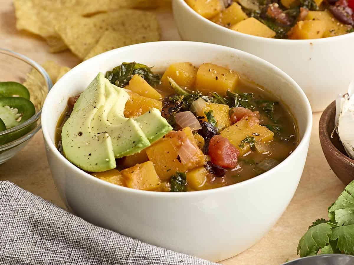 Vue latérale d'un bol de soupe de courge musquée et de haricots noirs, garnie de tranches d'avocat.