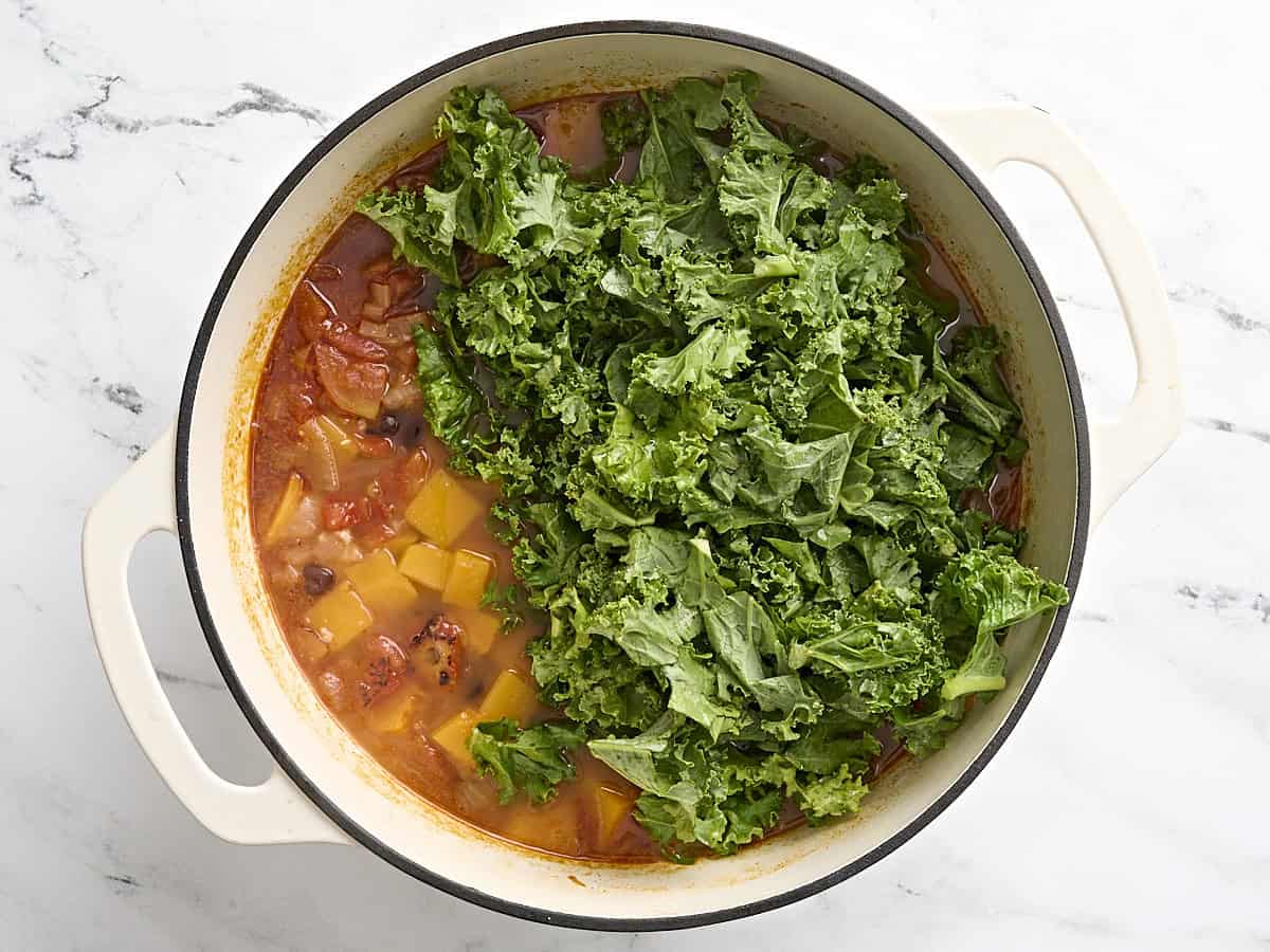 Chou haché ajouté à la courge musquée et à la soupe aux haricots noirs dans une cocotte.