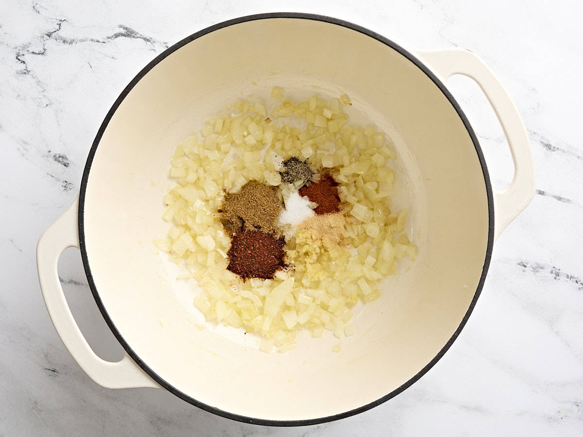Oignons coupés en dés avec de la poudre de chili, du cumin, de la poudre d'ail, du paprika fumé, du sel et du poivre noir fraîchement concassé ajoutés dans une cocotte.