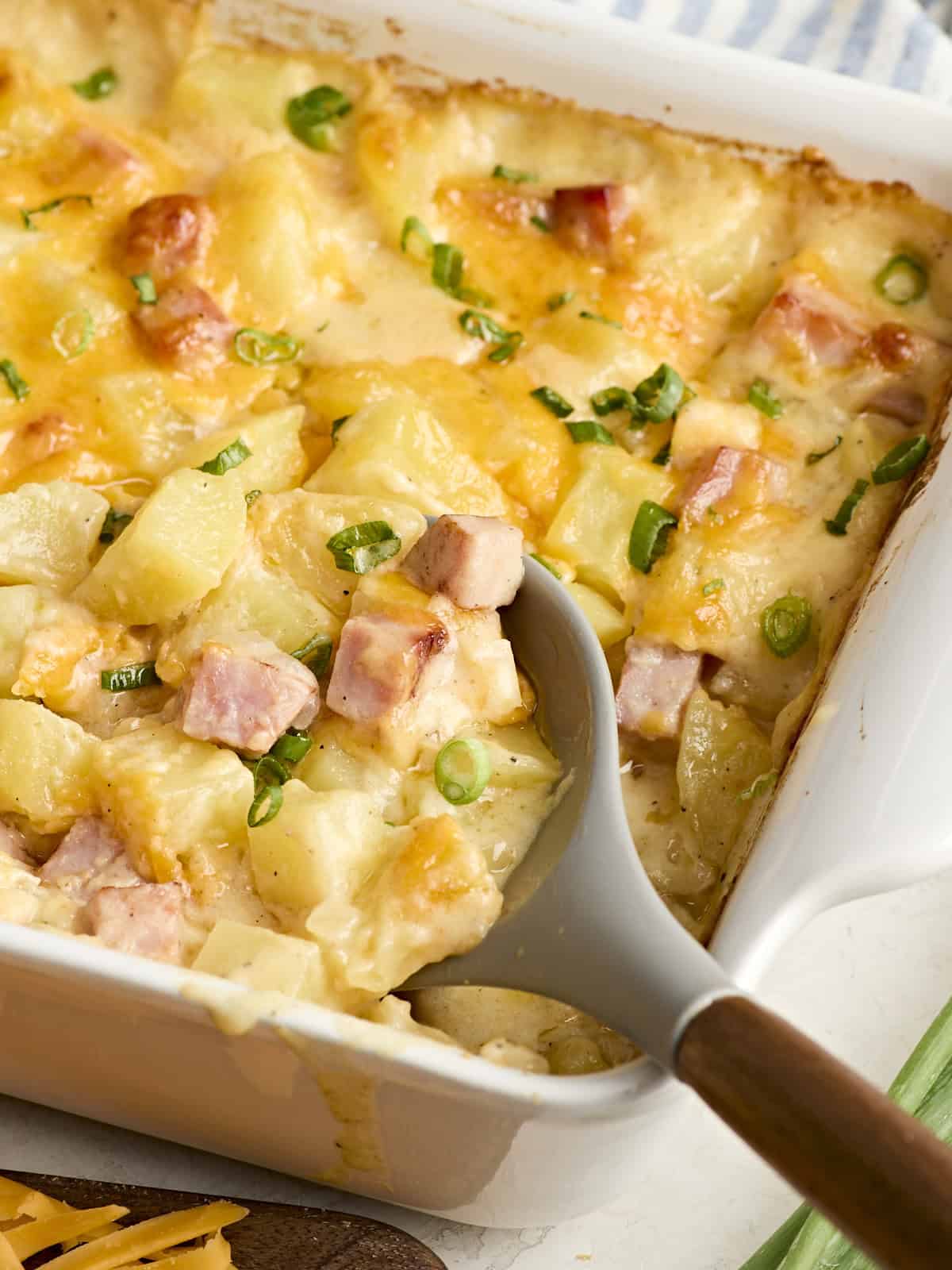 Une cuillère de service ramassant une cocotte de jambon et de pommes de terre dans un plat allant au four.