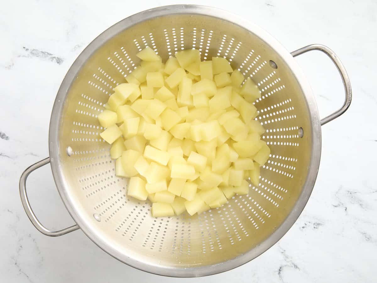 Pommes de terre coupées en dés égouttées dans une passoire.