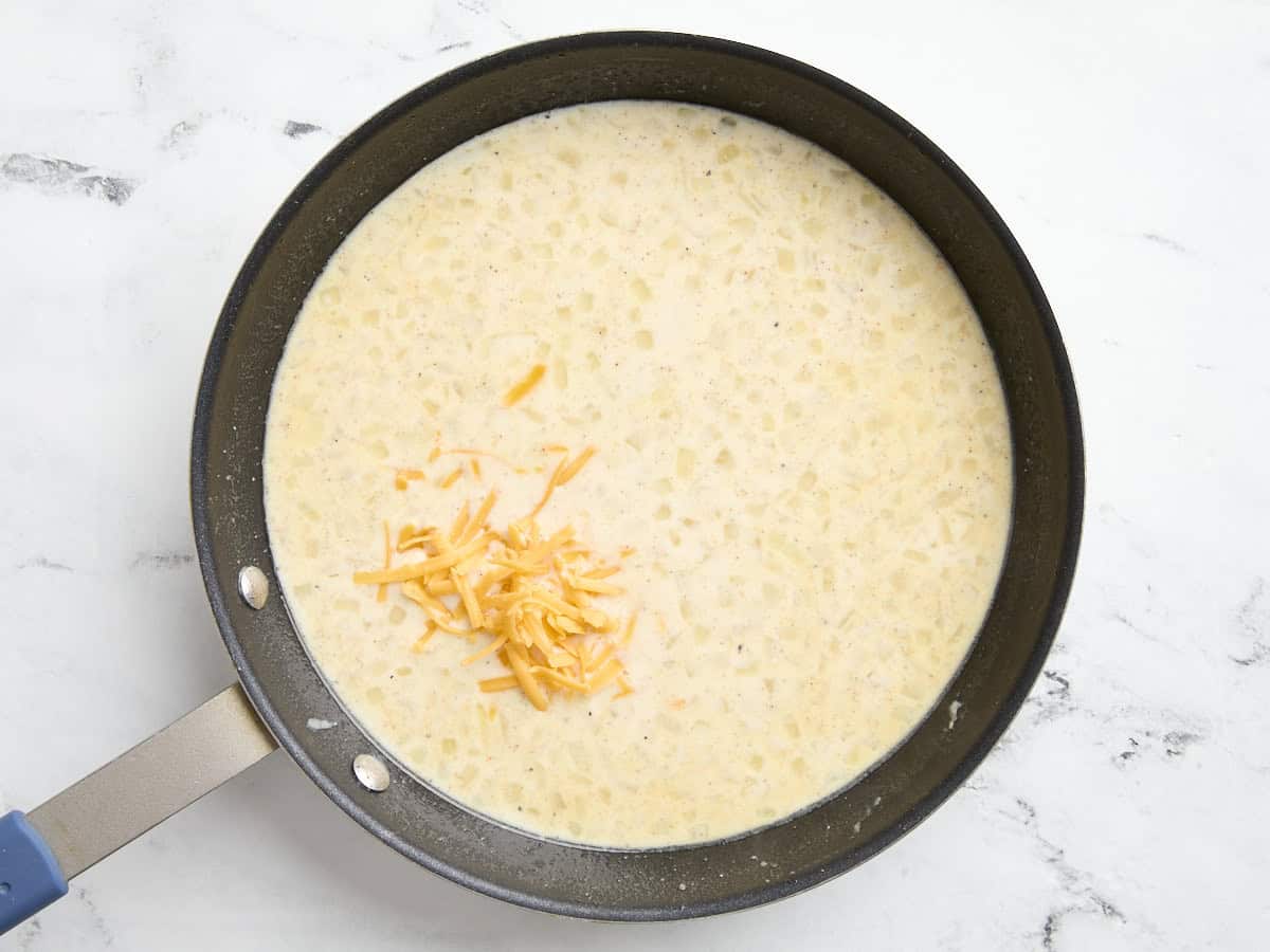 La sauce crémeuse pour la cocotte de jambon et de fromage dans une poêle avec du fromage râpé ajouté.