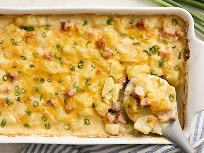 Vue aérienne d'une cuillère de service qui prélève une cocotte de jambon et de pommes de terre dans un plat allant au four.