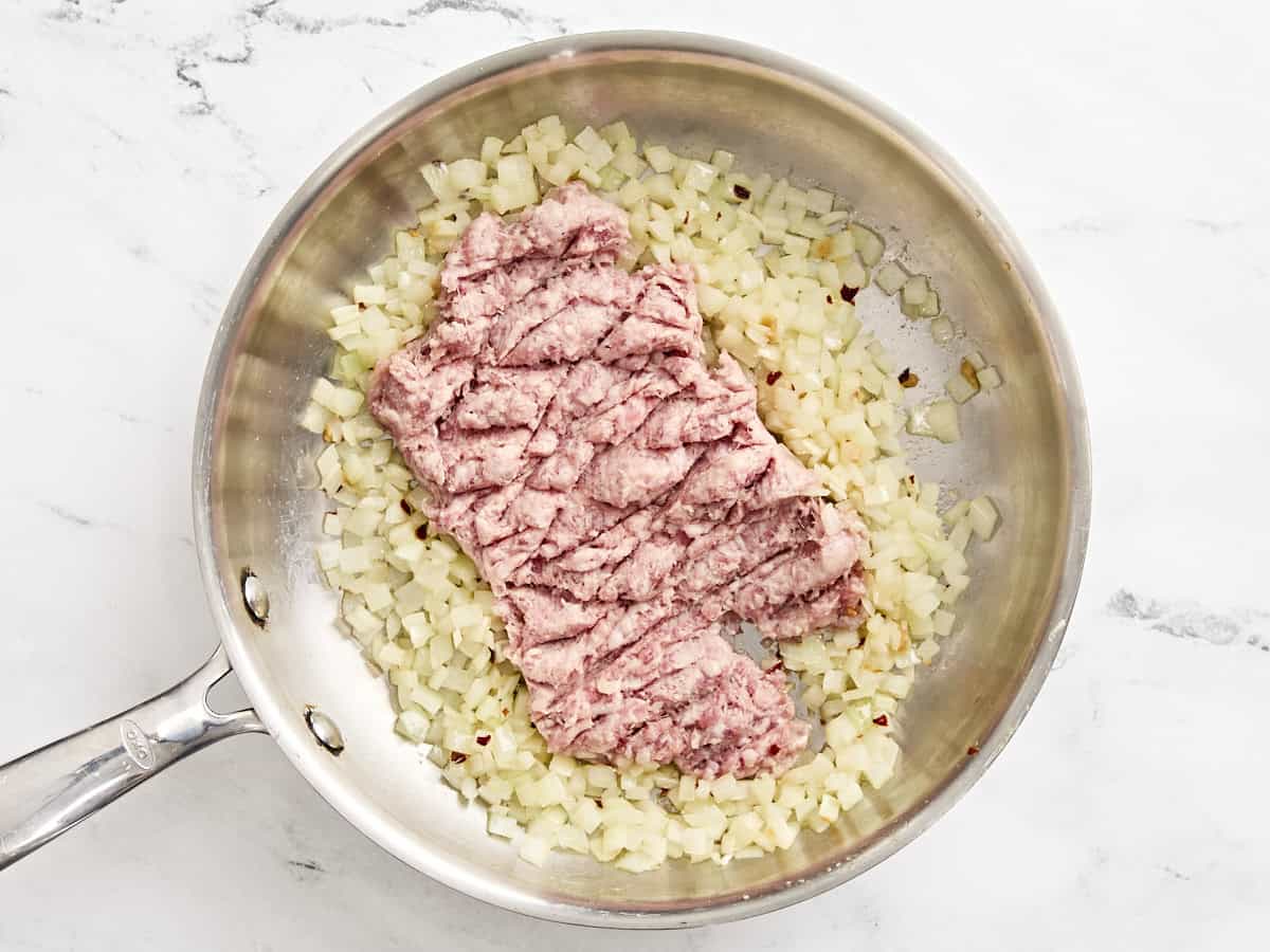 Saucisse hachée ajoutée à une poêle avec des oignons coupés en dés.