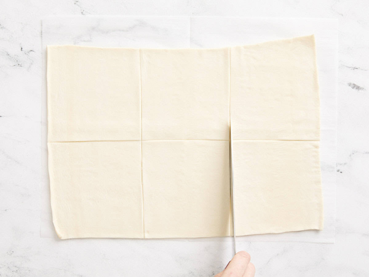 Un couteau coupant une feuille de pâte feuilletée en carré.