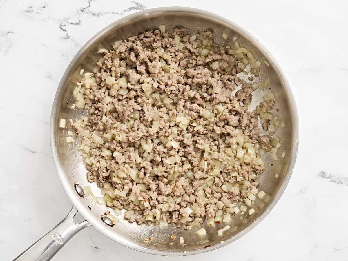 Cuisson des saucisses hachées et de l'oignon dans une poêle.
