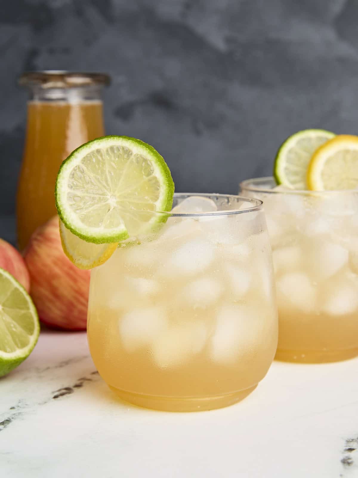 Vue latérale du cocktail sans alcool au cidre de pomme dans des verres, avec des tranches de citron et de lime comme garniture.