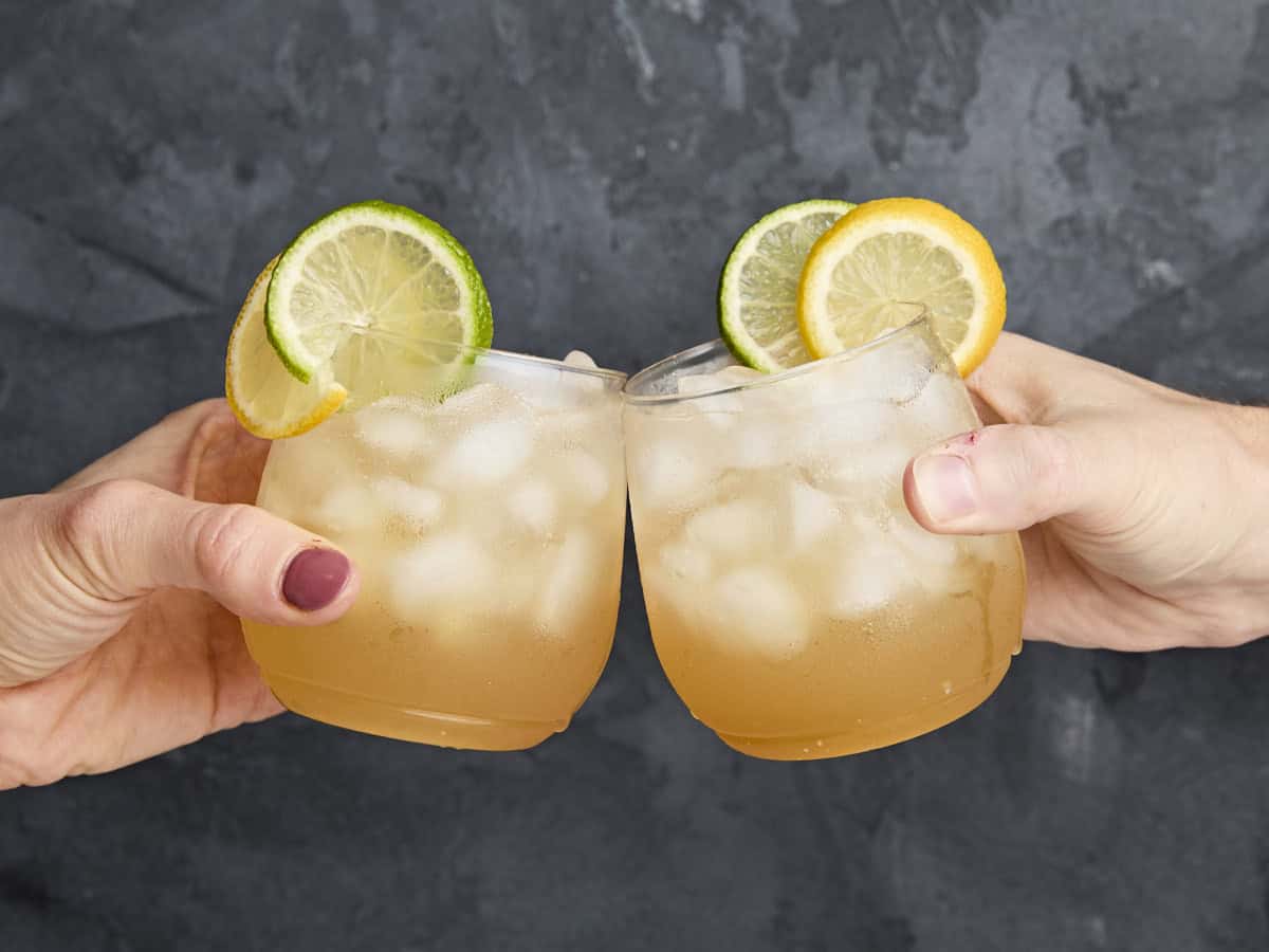 Deux mains tintent ensemble deux verres de Apple Cider Shrub Mocktail.