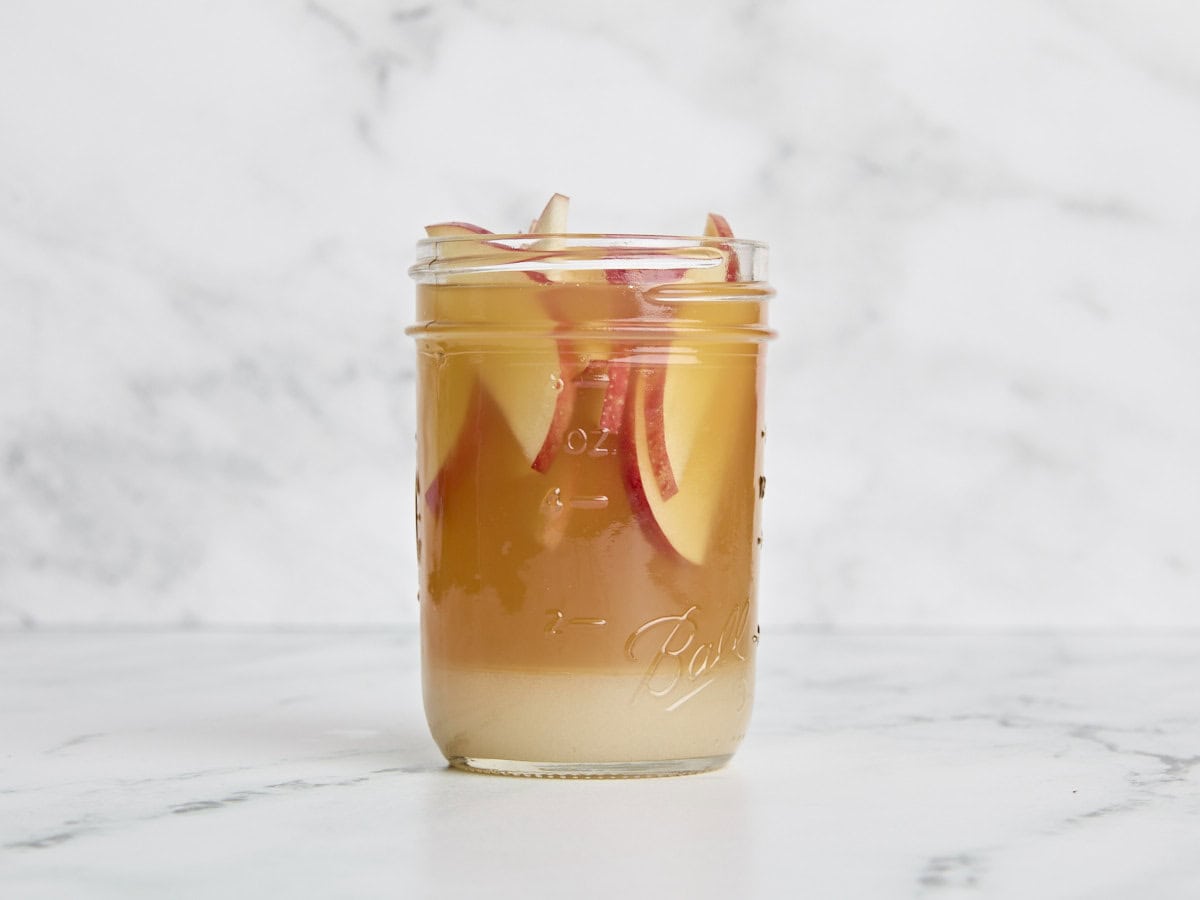 Pommes tranchées ajoutées à l'arbuste à cidre de pomme dans un bocal en verre.