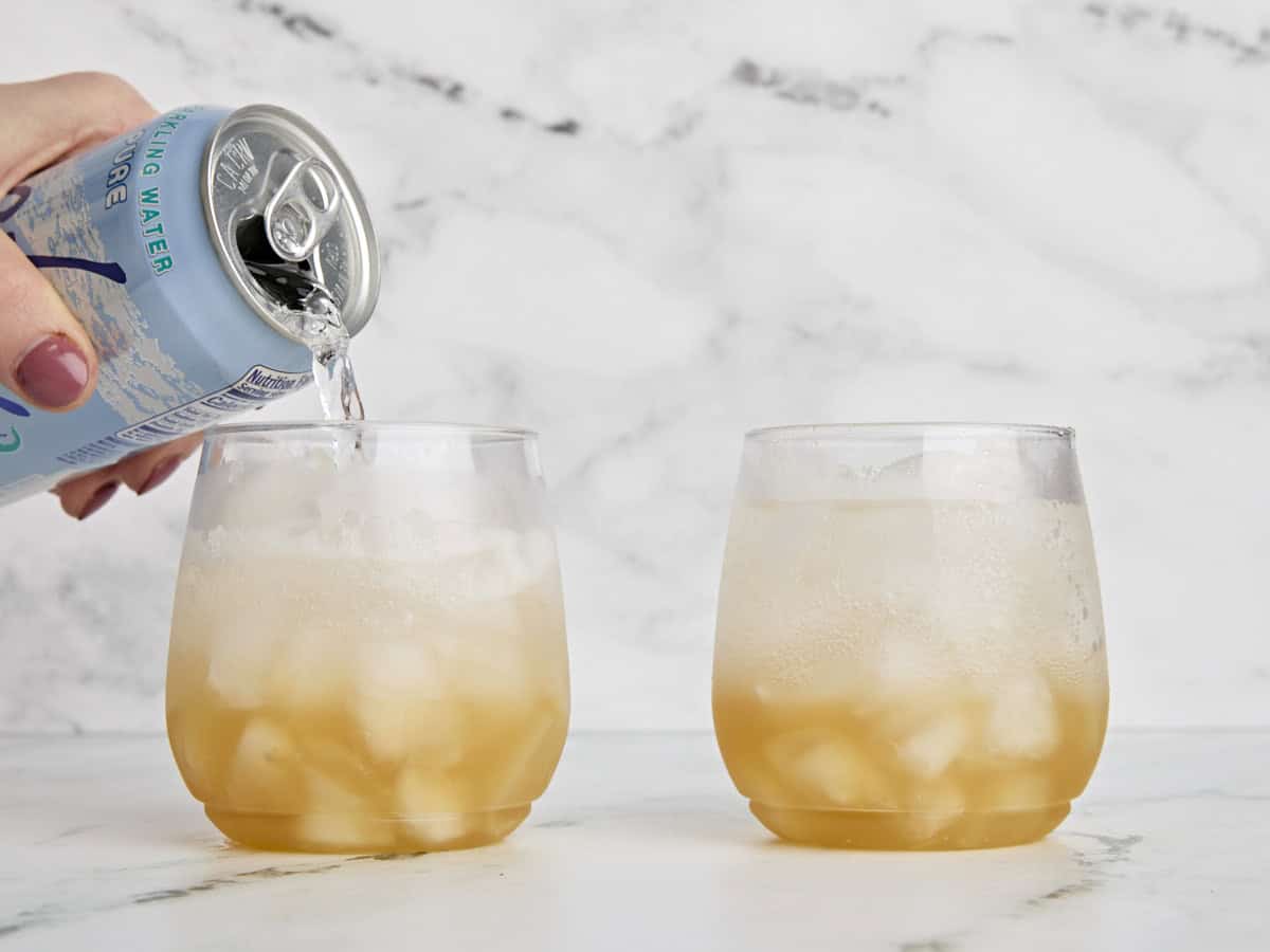 De l'eau gazeuse est versée dans un verre de glace avec du cidre de pomme pour faire un cocktail sans alcool.