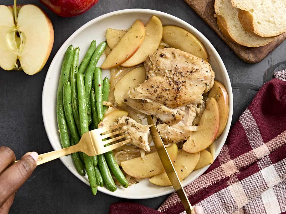 Vue aérienne du dîner à la poêle de poulet et de pommes coupé avec un couteau et une fourchette sur une assiette avec des haricots verts.