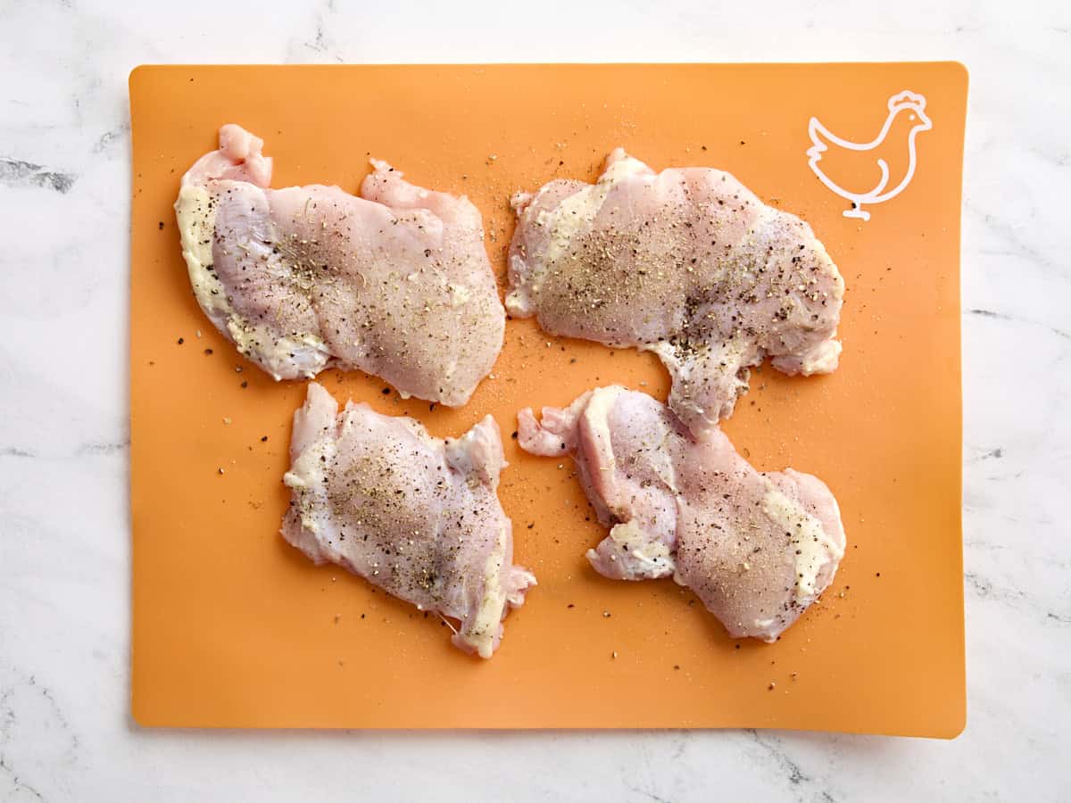 Cuisses de poulet assaisonnées sur un tapis de préparation culinaire.