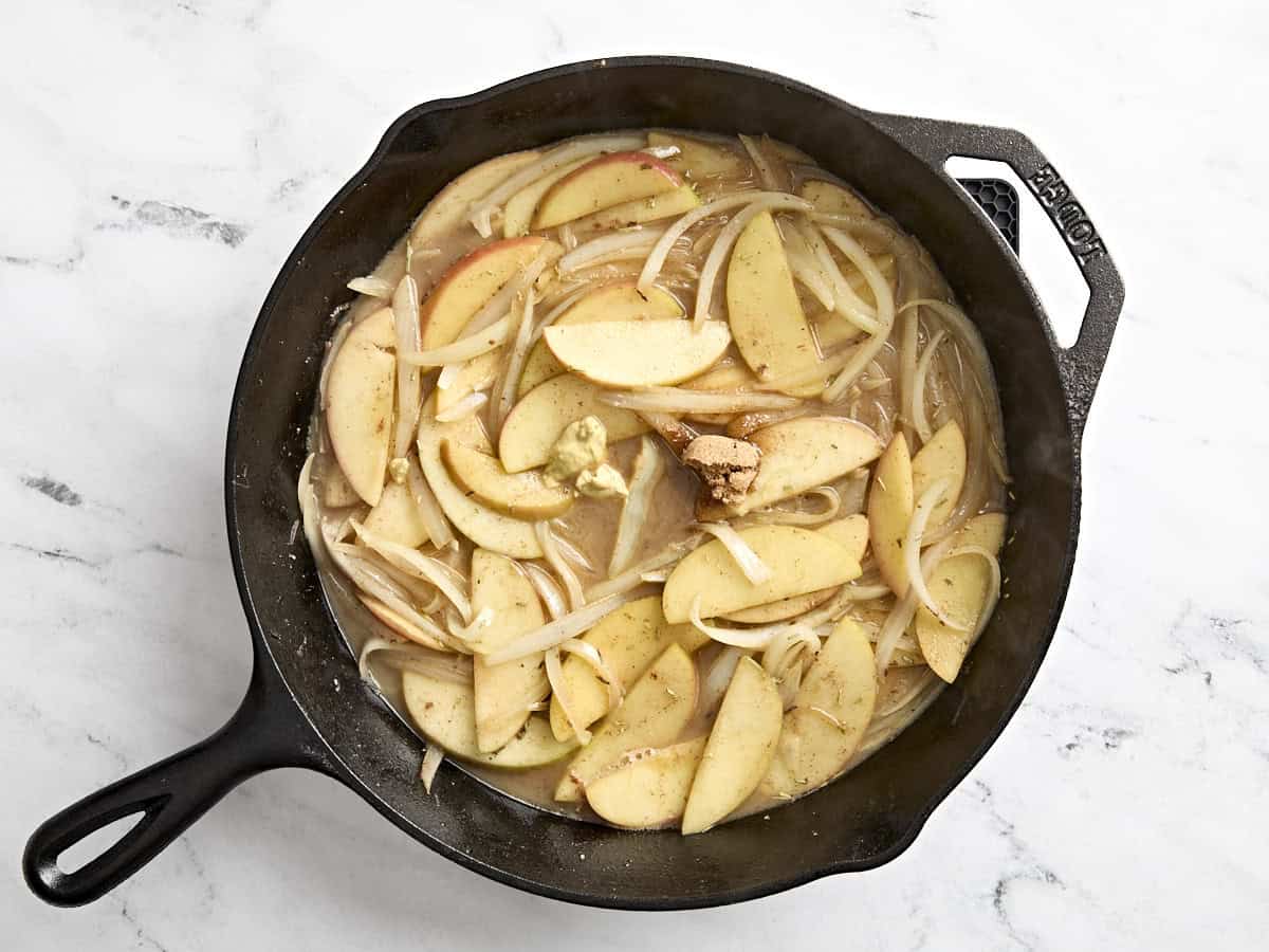Pommes et oignons tranchés cuisant dans une sauce au cidre de pomme dans une poêle.